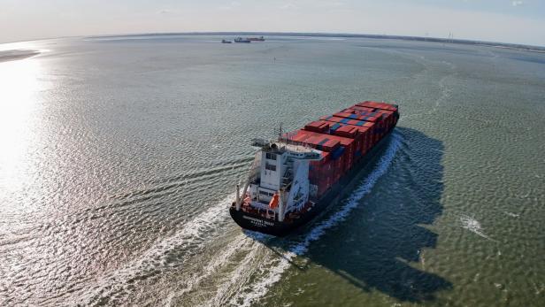 Ein großes Containerschiff fährt auf dem Meer, beladen mit vielen roten und blauen Containern.