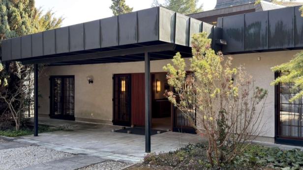 Eingangsbereich eines modernen Hauses mit Flachdach, großen Fenstern und umgebender Bepflanzung.