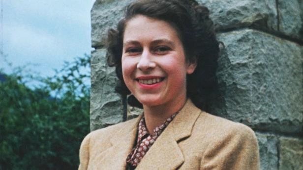 Die junge Queen Elizabeth lehnt an einer Steinmauer.