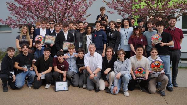 Eine große Gruppe junger Menschen und Erwachsener posiert mit Auszeichnungen vor blühenden Kirschbäumen.