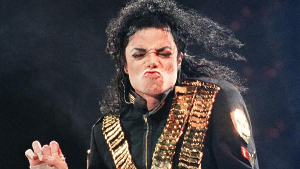 Michael Jackson tanzt mit schwarzer Jacke und goldenem Gürtel auf der Bühne.