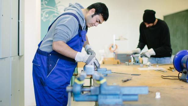 Zwei Männer arbeiten in einer Werkstatt mit Werkzeugen und Metallstücken.