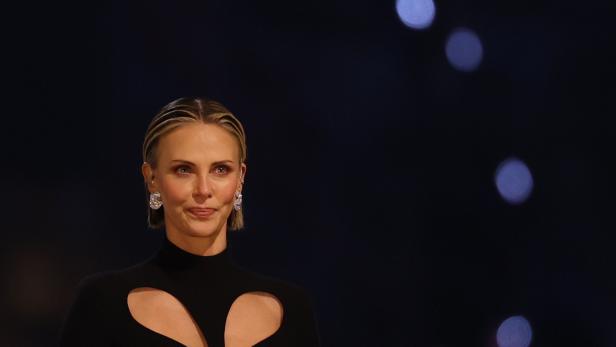 Charlize Theron trägt ein schwarzes Kleid mit Ausschnitten und auffälligen Ohrringen.
