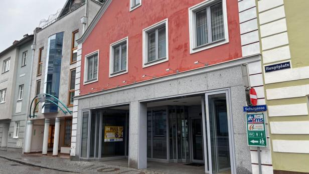 Mehrstöckiges Gebäude mit roter Fassade, mehreren Fenstern und einem offenen Eingang an einer gepflasterten Straße.