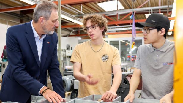 Drei Männer unterhalten sich in einer Werkstatt an einer Metallkonstruktion.