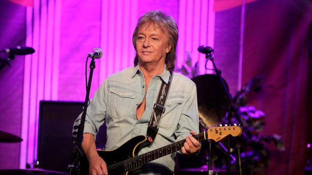 Chris Norman spielt Gitarre auf einer Bühne mit lila Hintergrundbeleuchtung.