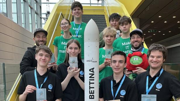 Eine Gruppe junger Menschen steht auf einer Treppe um eine Modellrakete und hält Auszeichnungen in den Händen.