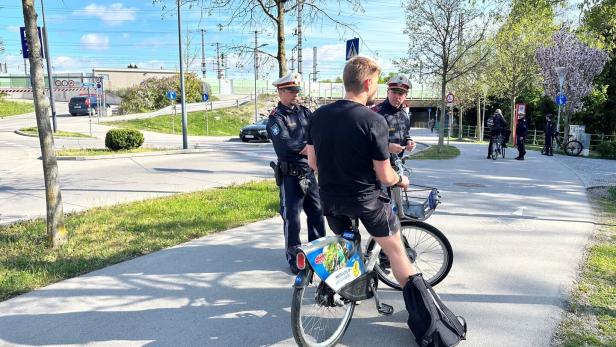 Ein Radfahrer wird von zwei Polizisten auf einem Weg angehalten.