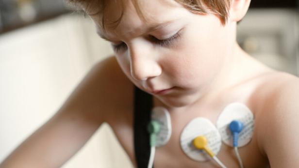 Ein Junge mit Elektroden auf der Brust hält Tabletten in der Hand und blickt nachdenklich darauf.