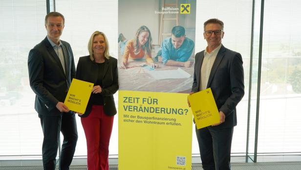 Drei Personen in Businesskleidung stehen neben einem Werbebanner der Raiffeisen Bausparkasse und halten gelbe Mappen.