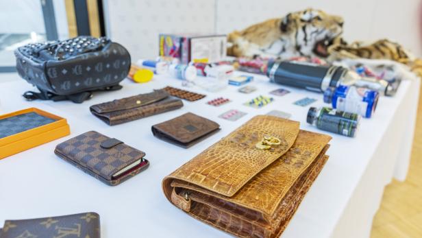 Auf einem Tisch liegen diverse Geldbörsen, Pillen, ein Tigerfell und andere Gegenstände.