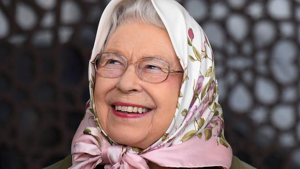 Eine lächelnde Queen Elizabeth mit Brille und einem geblümten Kopftuch schaut zur Seite.