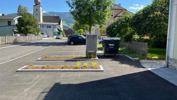 Frisch asphaltierter Parkplatz mit bepflanzten Grüninseln und umliegenden Gebäuden bei Sonnenschein.