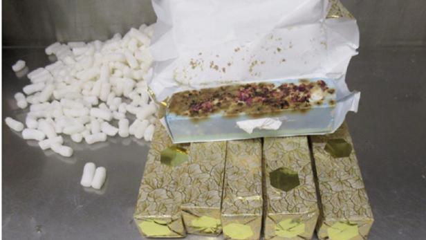 Eine offene Packung Seife mit Blüten liegt auf goldenen, blattgemusterten Schachteln, neben Verpackungschips.