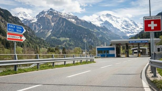 Eine Straße vor Bergen, rechts die Flagge der Schweiz 