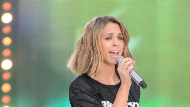 Vanessa Mai mit kurzem, blondem Haar singt in einem schwarzen Sporttrikot ins Mikrofon.
