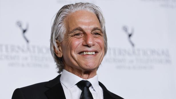 Ein lächelnder Tony Danza trägt einen schwarzen Anzug mit Krawatte und ein Friedenssymbol-Anstecknadel.