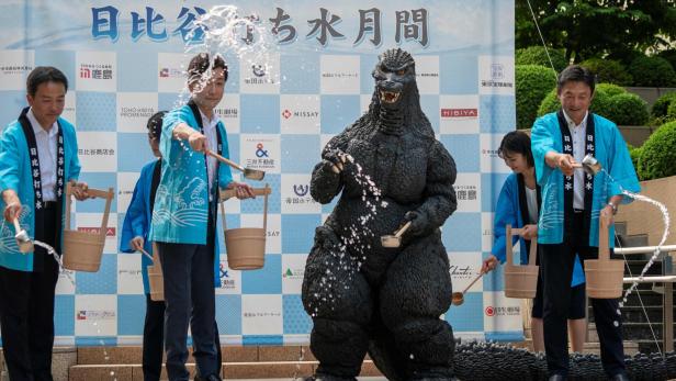Japaner mit Godzilla-Statue bei einem Event.