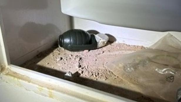 Eine Handgranate liegt auf staubigem Untergrund in einem offenen Fach neben einer durchsichtigen Plastiktüte.