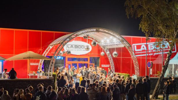 Viele Menschen stehen abends vor dem rot beleuchteten Eingang des Nachtclubs La Boom in St. Pölten.