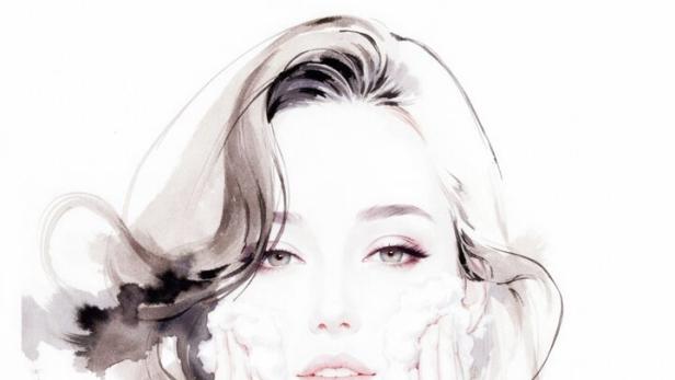 Eine Frau mit schulterlangem Haar wäscht ihr Gesicht mit Schaum und trägt ein schwarzes Oberteil.