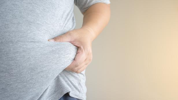 Eine Person hält mit der Hand ihren Bauch, der von einem grauen T-Shirt bedeckt ist.