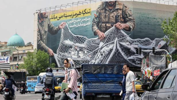 Eine belebte Straße in Teheran mit einem großen Plakat, das Soldaten mit einem Netz voller Flugzeuge zeigt.