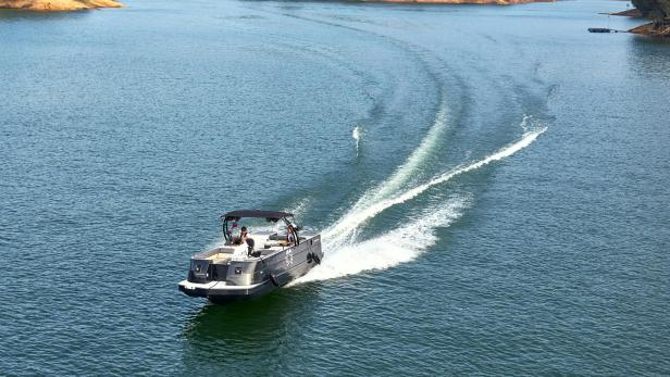 Motorboot fährt auf einem ruhigen See, im Hintergrund bewaldetes Ufer.