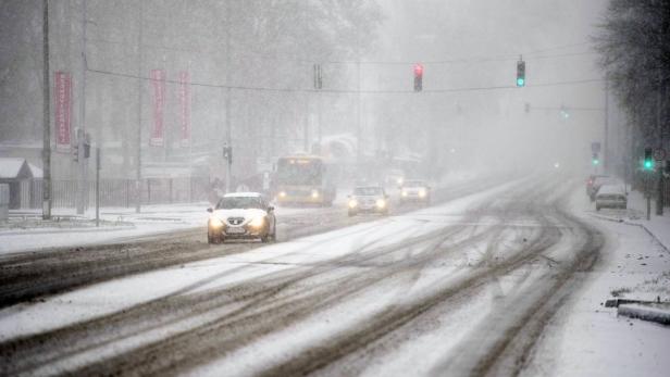 Autos und ein Bus fahren auf einer verschneiten Straße bei starkem Schneefall.