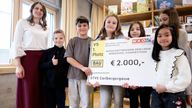 Kindergruppe mit Lehrerin hält Siegerscheck der Miniziegel-Competition in einem Klassenraum.