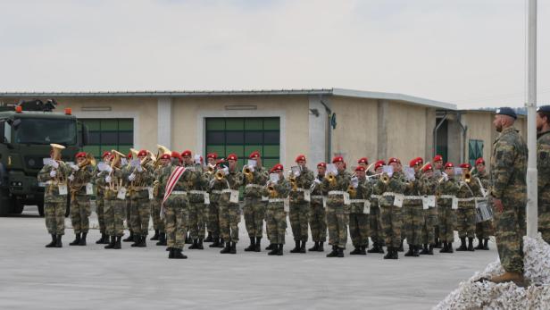 Militärmusiker in Tarnuniform und roten Baretten spielen auf dem Hof einer Kaserne.