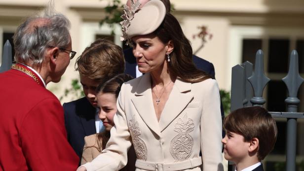 Prinzessin Kate, mit Hut und Kindern, schüttelt einem Mann in roter Robe die Hand.
