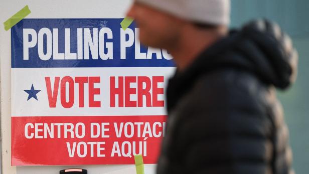 Ein Mann mit Mütze geht an einem Schild vorbei, das auf Englisch und Spanisch zum Wählen auffordert.
