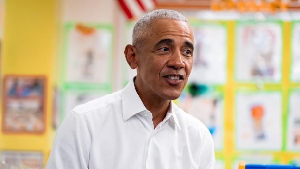 Barack Obama lächelt in einem hellen Raum mit Kinderzeichnungen im Hintergrund.