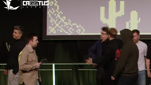 Mehrere junge Männer auf einer Bühne, einer schlägt einem anderen ins Gesicht, Publikum im Hintergrund.