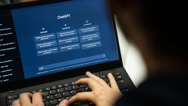 Eine Person tippt auf einer Tastatur vor einem Laptop, auf dem die ChatGPT-Oberfläche geöffnet ist.