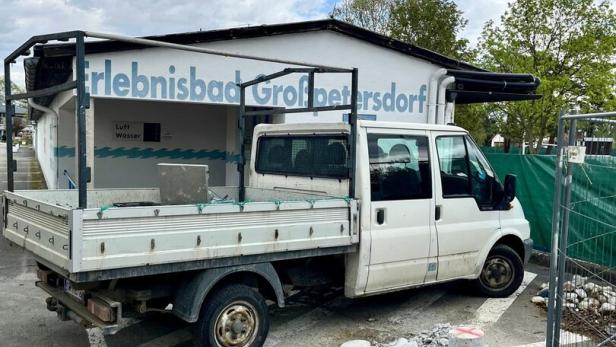 Ein weißer Transporter steht vor einem Gebäude mit der Aufschrift „Erlebnisbad Großpetersdorf“, daneben liegen Bauschutt und Steine.