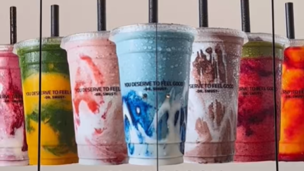 Mehrere bunte Smoothies in Plastikbechern mit Strohhalmen vor dem Schriftzug "Dr. Smusy Vienna".