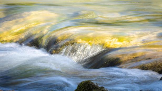 Fließendes Wasser mit kleinen Wellen und Felsen im Vordergrund