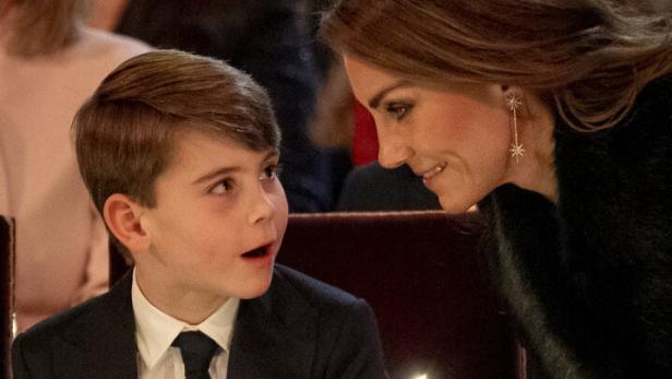 Prinzessin Kate und Prinz Louis im Anzug sitzen nebeneinander, halten Kerzen und lächeln sich während einer festlichen Zeremonie an.