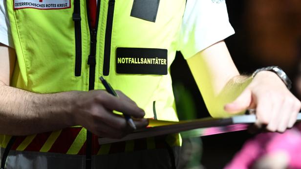 Eine Person in einer gelben Notfallsanitäter-Weste schreibt mit einem Stift auf ein Klemmbrett.