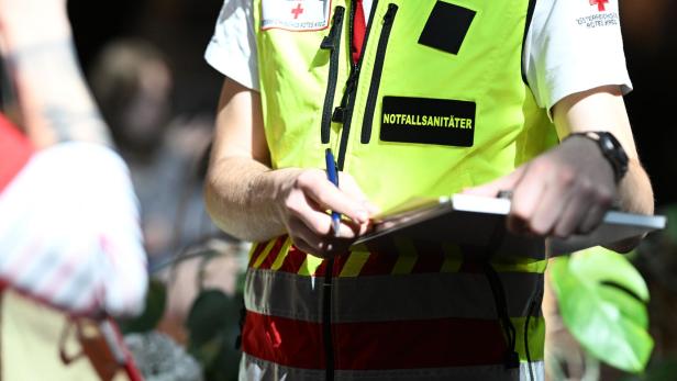 Ein Notfallsanitäter mit gelber Weste schreibt mit einem Stift auf ein Klemmbrett.