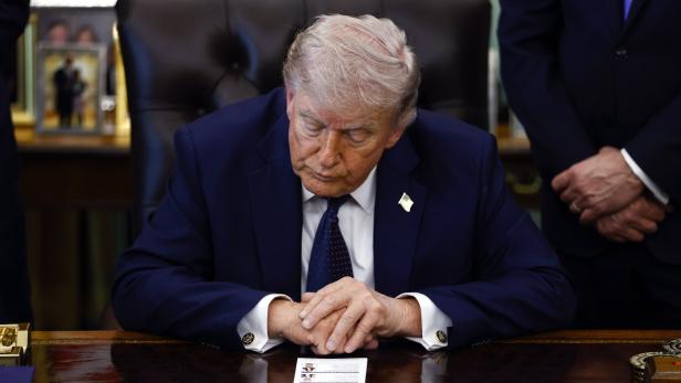Donald Trump sitzt am Schreibtisch und betrachtet ein Dokument.