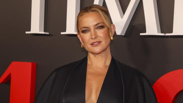 Kate Hudson trägt ein schwarzes Kleid vor einem Hintergrund mit roten und weißen Elementen.