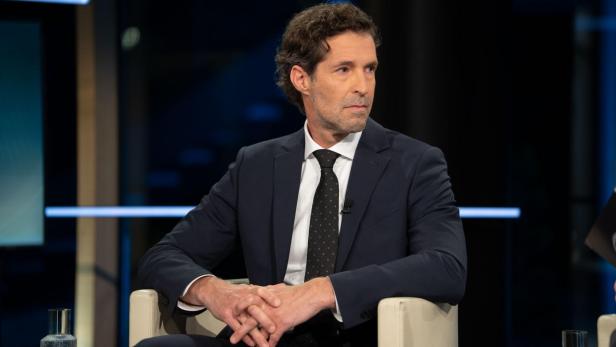 Mann in dunklem Anzug in TV-Studio sitzend