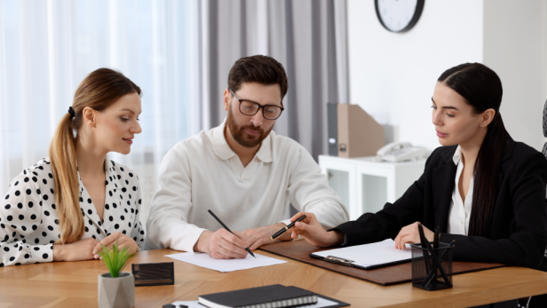 Ein Paar unterschreibt etwas, eine Notarin sitzt neben dran 