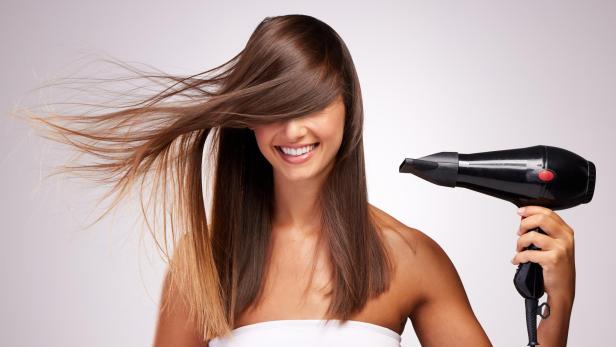 Eine Frau fönt sich die Haare vor weißem Hintergrund