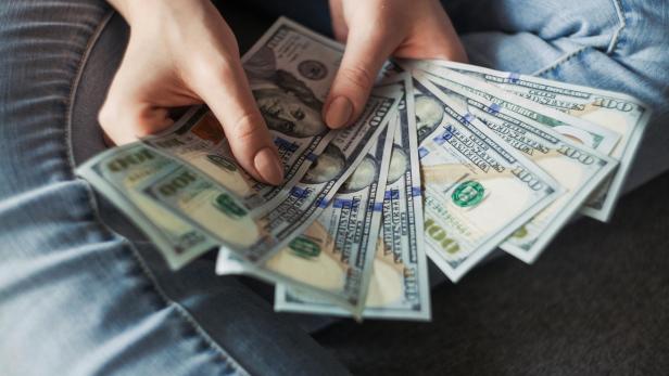 Eine junge Frau hält Dollar-Scheine in den Händen, während ihre Füße überkreuzt sind.