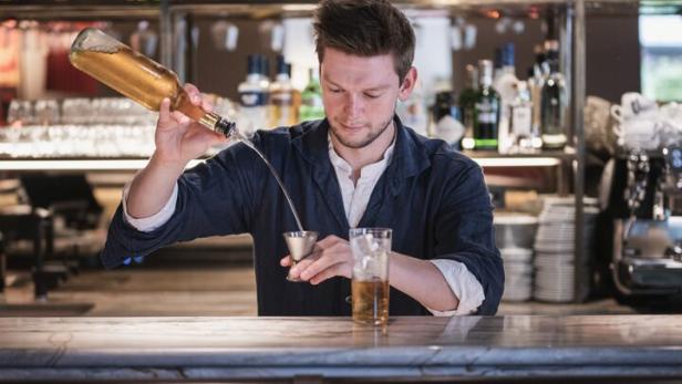 Ein Barkeeper gießt eine Flüssigkeit aus einer Flasche in einen Messbecher an einer Bar.