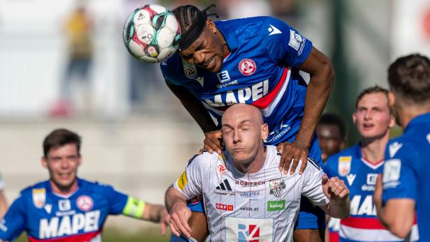 Ein GAK-Spieler stützt sich beim Kopfballduell auf den Schultern eines WAC-Spielers auf.
